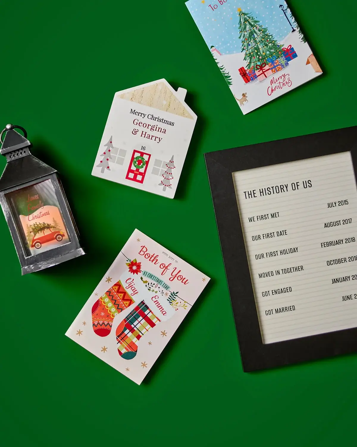 Christmas gift collection featuring personalised cards, a festive lantern, a personalised house decoration, and a framed keepsake print on a green background.